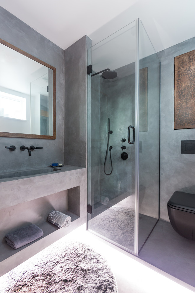 Small urban ensuite bathroom in London with beaded cabinets, brown cabinets, a walk-in shower, a wall mounted toilet, grey tiles, grey walls, concrete flooring, a wall-mounted sink, grey floors and a hinged door.