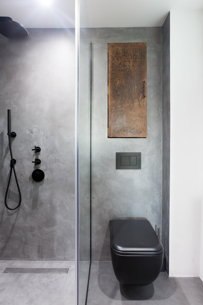Foto på ett litet industriellt en-suite badrum, med luckor med profilerade fronter, bruna skåp, en öppen dusch, en vägghängd toalettstol, grå kakel, grå väggar, betonggolv, ett väggmonterat handfat, grått golv och dusch med gångjärnsdörr