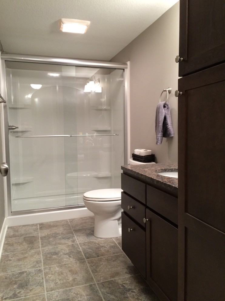 Cette photo montre une salle de bain chic en bois foncé de taille moyenne avec un placard avec porte à panneau encastré, un mur gris, un sol en carrelage de porcelaine, un lavabo encastré et un plan de toilette en granite.