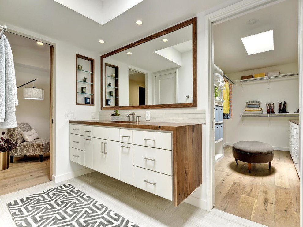 Cette image montre une salle de bain principale minimaliste de taille moyenne avec un placard à porte plane, des portes de placard blanches, un carrelage beige, des carreaux de céramique, un mur blanc, un sol en carrelage de céramique, un lavabo encastré et un plan de toilette en bois.