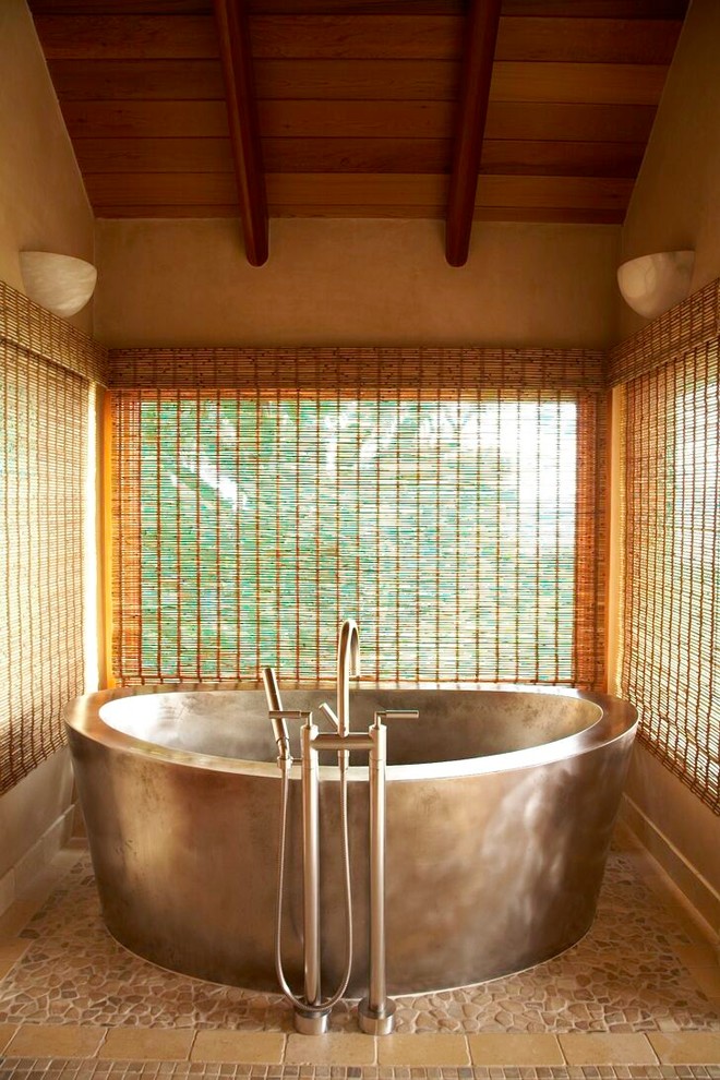 Immagine di una stanza da bagno tropicale con vasca freestanding e piastrelle in pietra