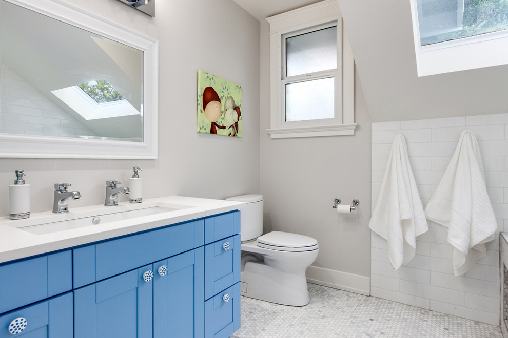 Modelo de cuarto de baño infantil tradicional renovado de tamaño medio con lavabo bajoencimera, armarios estilo shaker, puertas de armario azules, baldosas y/o azulejos blancos, paredes grises, bañera empotrada, ducha empotrada y baldosas y/o azulejos en mosaico