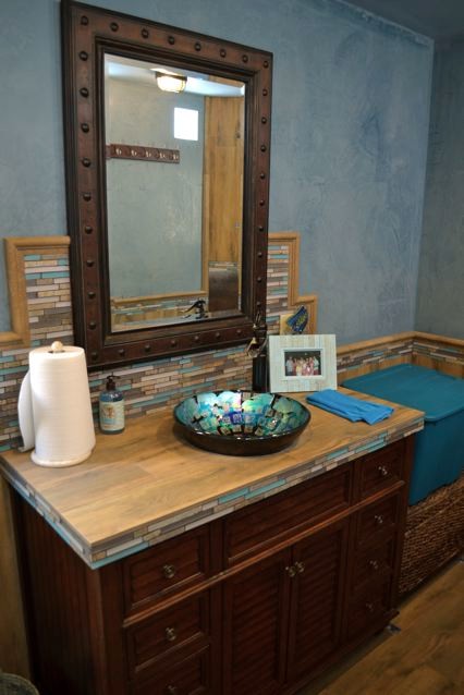 Aménagement d'une petite salle d'eau bord de mer en bois brun avec un placard à porte persienne, un carrelage multicolore, mosaïque, une douche d'angle, WC à poser, une vasque, un mur bleu, un sol en bois brun et un plan de toilette en bois.