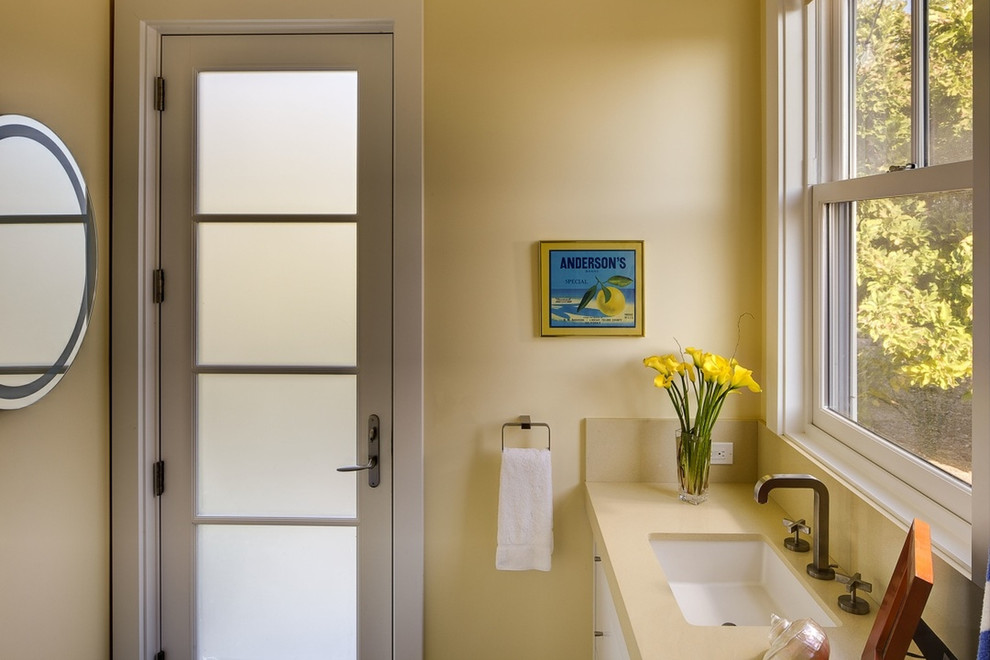 Landhausstil Badezimmer mit flächenbündigen Schrankfronten, weißen Schränken, beigen Fliesen, gelber Wandfarbe, Unterbauwaschbecken und Mineralwerkstoff-Waschtisch in San Francisco