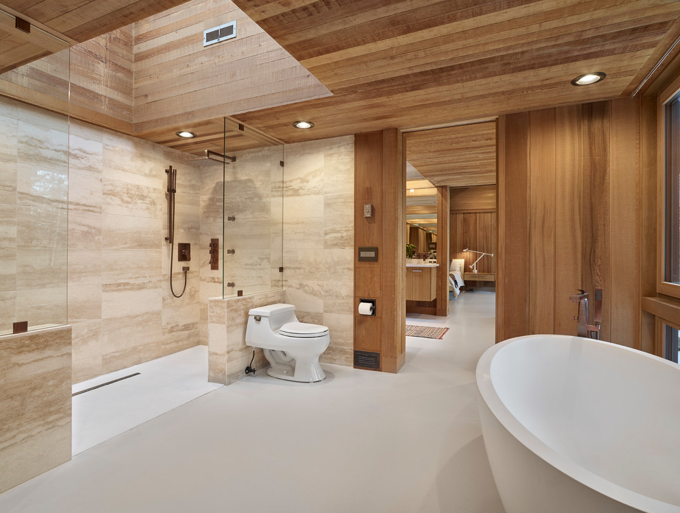 Стильный дизайн: огромная главная ванная комната в стиле модернизм с отдельно стоящей ванной, душевой комнатой, унитазом-моноблоком, бежевой плиткой, каменной плиткой, коричневыми стенами, бетонным полом, серым полом, плоскими фасадами, светлыми деревянными фасадами, врезной раковиной, столешницей из искусственного камня и открытым душем - последний тренд
