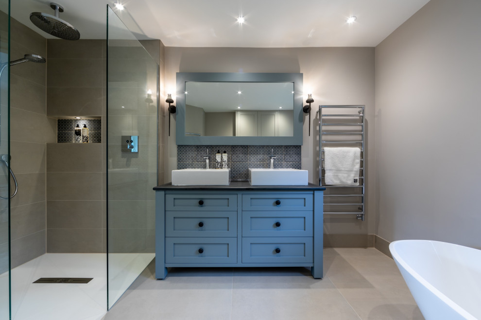 Medium sized classic ensuite bathroom in Surrey with shaker cabinets, blue cabinets, a freestanding bath, a corner shower, grey tiles, porcelain tiles, grey walls, porcelain flooring, a vessel sink, grey floors, black worktops, double sinks, a wall niche and a freestanding vanity unit.