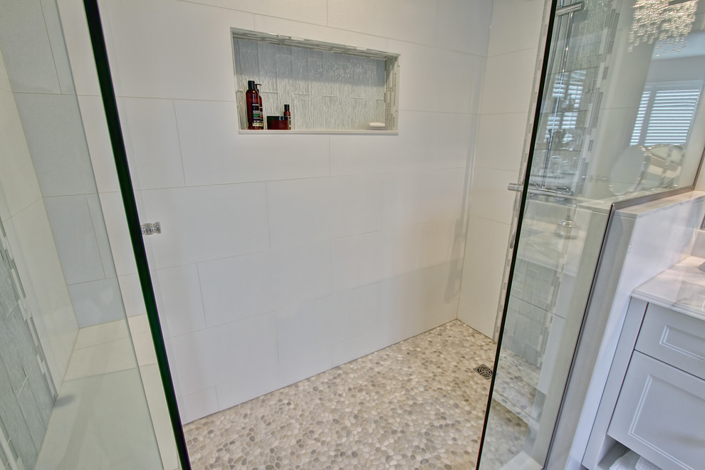 На фото: ванная комната среднего размера в стиле неоклассика (современная классика) с душем в нише, белой плиткой, керамогранитной плиткой, белыми стенами, полом из галечной плитки, фасадами с утопленной филенкой, белыми фасадами и столешницей из искусственного камня