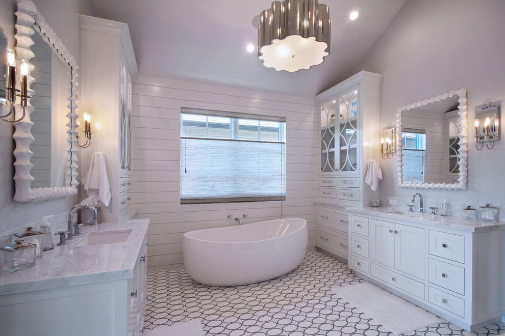 Cette photo montre une salle de bain chic avec un lavabo encastré, un placard à porte shaker, des portes de placard blanches, un plan de toilette en marbre, une baignoire indépendante, un carrelage blanc et un mur blanc.