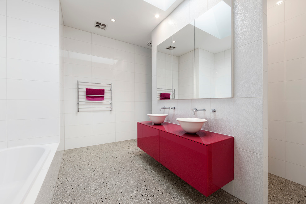 На фото: большая детская ванная комната в современном стиле с плоскими фасадами, красными фасадами, накладной ванной, душем в нише, инсталляцией, белой плиткой, керамической плиткой, белыми стенами, бетонным полом, настольной раковиной и столешницей из искусственного камня с