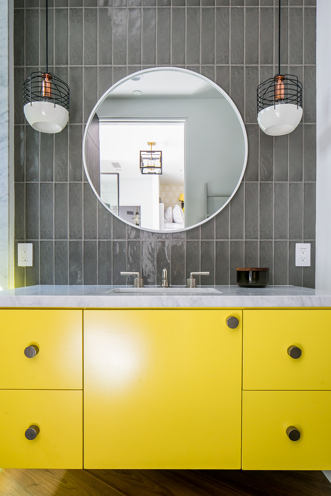 Modernes Duschbad mit flächenbündigen Schrankfronten, gelben Schränken, grauen Fliesen, Glasfliesen, grauer Wandfarbe, braunem Holzboden, Unterbauwaschbecken, braunem Boden und weißer Waschtischplatte in Orange County
