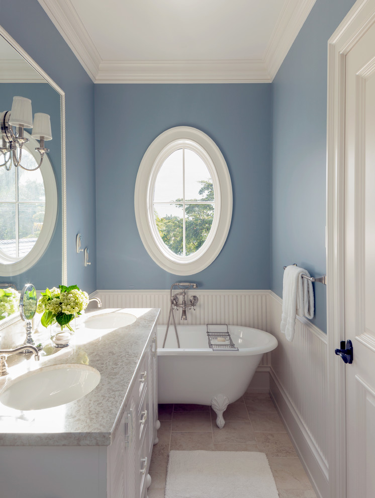 Maritim inredning av ett stort badrum med dusch, med luckor med infälld panel, vita skåp, granitbänkskiva, ett badkar med tassar, grå kakel, stenkakel, blå väggar, marmorgolv och ett undermonterad handfat
