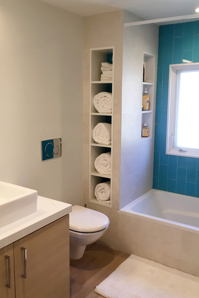 Пример оригинального дизайна: ванная комната в стиле неоклассика (современная классика) с плоскими фасадами, светлыми деревянными фасадами, душем над ванной, синей плиткой, стеклянной плиткой, бежевыми стенами, настольной раковиной, ванной в нише, унитазом-моноблоком, паркетным полом среднего тона, коричневым полом и шторкой для ванной