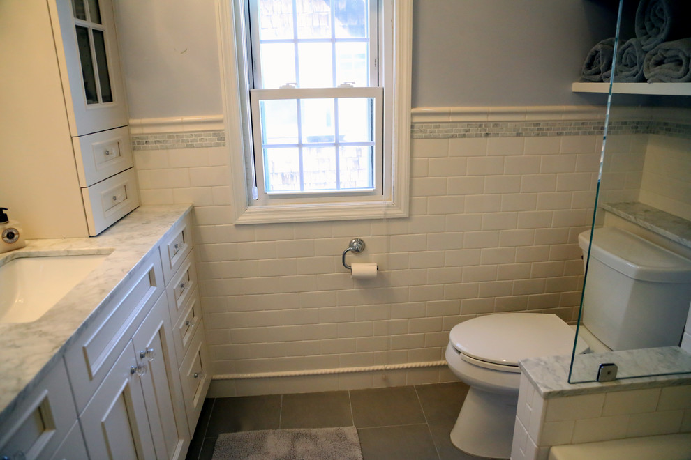 Bild på ett mellanstort vintage en-suite badrum, med möbel-liknande, vita skåp, ett badkar i en alkov, en toalettstol med separat cisternkåpa, vit kakel, keramikplattor, grå väggar, klinkergolv i porslin, ett undermonterad handfat och marmorbänkskiva