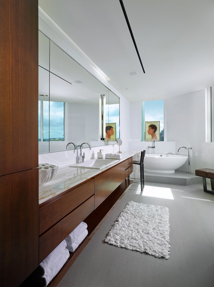 Imagen de cuarto de baño principal contemporáneo grande con puertas de armario de madera oscura, bañera exenta, baldosas y/o azulejos grises, paredes blancas, encimera de mármol y armarios con paneles lisos