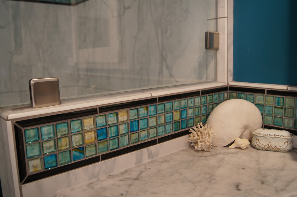 Bild på ett badrum, med ett undermonterad handfat, marmorbänkskiva, vit kakel och en dubbeldusch