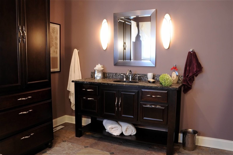 Cette photo montre une salle d'eau chic en bois foncé de taille moyenne avec un placard avec porte à panneau surélevé, un mur rose, un sol en carrelage de céramique, un lavabo encastré, un plan de toilette en granite et un sol marron.