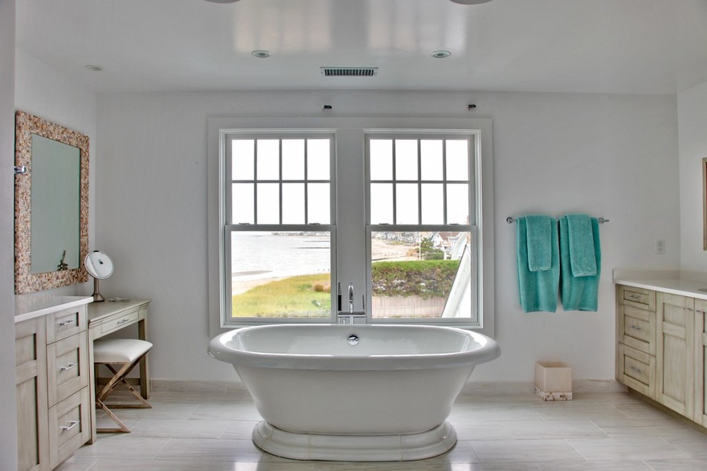 Modelo de cuarto de baño marinero con lavabo bajoencimera, puertas de armario grises, bañera exenta, paredes blancas, armarios con paneles lisos, encimera de cuarzo compacto y suelo de mármol
