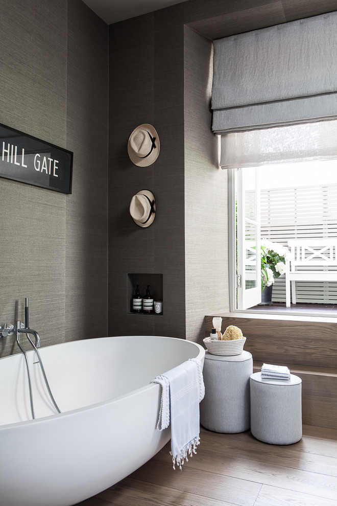 Modelo de cuarto de baño principal contemporáneo con bañera exenta, paredes grises, suelo de madera en tonos medios y ventanas