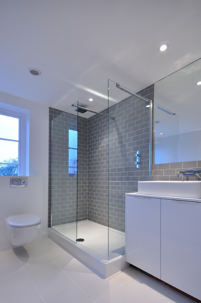 Design ideas for a medium sized contemporary bathroom in London with a vessel sink, flat-panel cabinets, white cabinets, a corner shower, a wall mounted toilet, grey tiles, metro tiles and white walls.