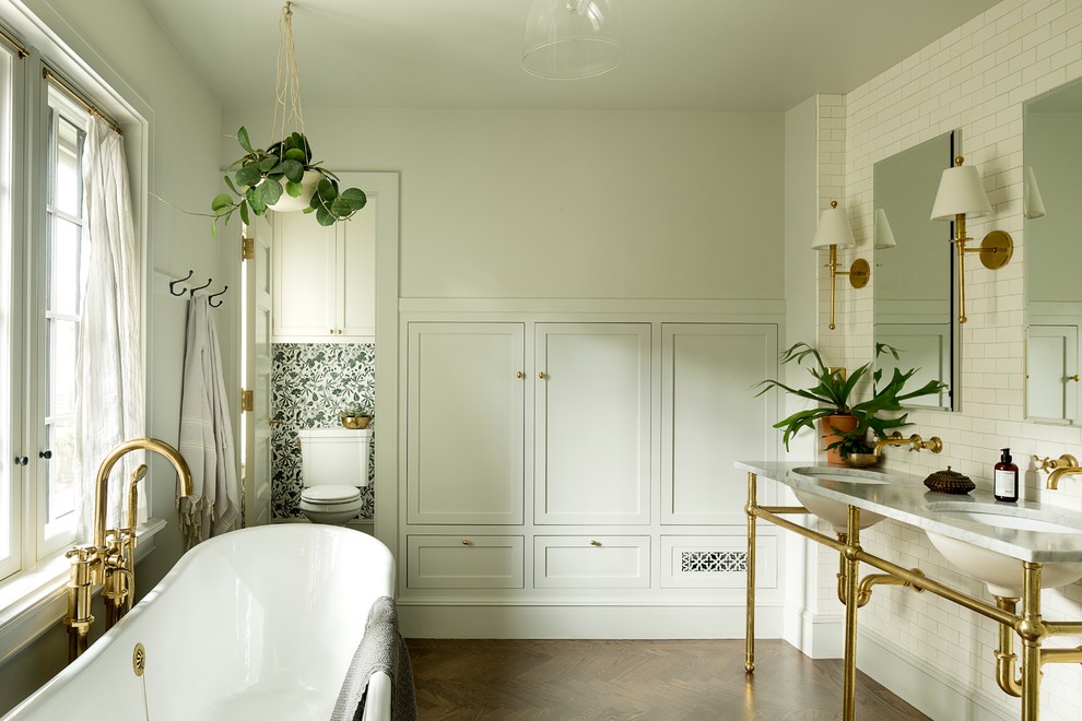 Aménagement d'une salle de bain principale classique de taille moyenne avec une baignoire indépendante, un carrelage blanc, un carrelage métro, un mur gris, parquet foncé, un lavabo encastré, un sol marron et un plan de toilette en marbre.