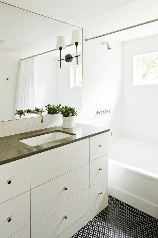 Immagine di una stanza da bagno contemporanea con lavabo sottopiano, ante lisce, ante bianche, vasca ad alcova, vasca/doccia e pavimento nero
