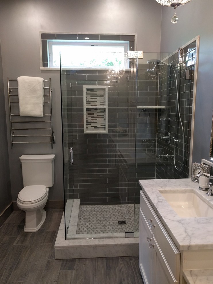 Photo of a medium sized traditional ensuite bathroom in San Diego with recessed-panel cabinets, distressed cabinets, a corner shower, a two-piece toilet, grey tiles, glass tiles, grey walls, ceramic flooring, a submerged sink, marble worktops, grey floors, a hinged door and a freestanding bath.
