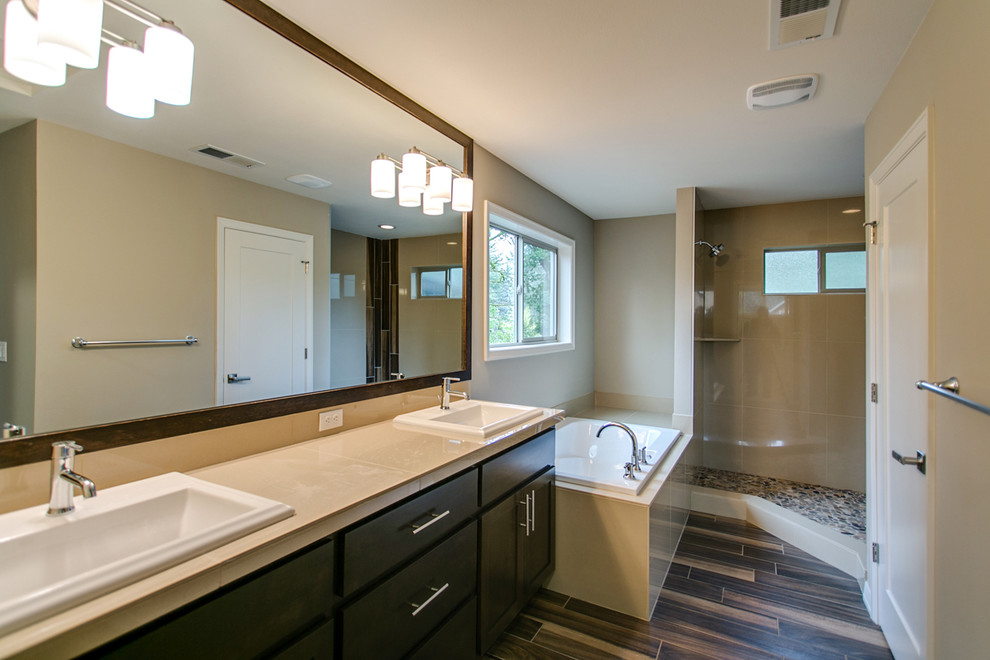 Inspiration for a medium sized contemporary ensuite bathroom in Portland with a built-in sink, recessed-panel cabinets, dark wood cabinets, a built-in bath, a corner shower, a two-piece toilet, beige tiles, pebble tiles, beige walls, ceramic flooring, solid surface worktops, brown floors and an open shower.