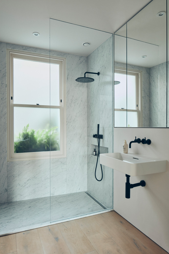 Cette photo montre une salle de bain principale tendance avec une douche à l'italienne, un carrelage blanc, des dalles de pierre, un mur blanc, un sol en bois brun, un lavabo suspendu, un sol marron, aucune cabine et WC suspendus.
