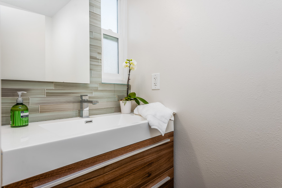 Foto på ett litet maritimt vit badrum, med släta luckor, skåp i mellenmörkt trä, beige kakel, brun kakel, grå kakel, glaskakel, grå väggar, ett integrerad handfat och bänkskiva i akrylsten