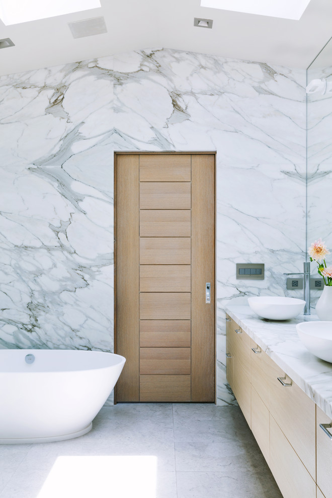 Photo of a contemporary bathroom in San Francisco with flat-panel cabinets, light wood cabinets, a freestanding bath, travertine flooring, marble worktops, grey floors, white worktops and a vessel sink.