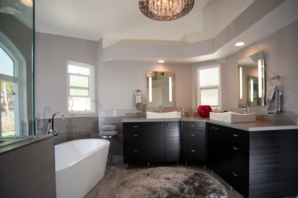 Exemple d'une grande salle de bain principale tendance en bois foncé avec un placard à porte plane, une baignoire indépendante, une douche d'angle, WC séparés, un carrelage gris, des carreaux de porcelaine, un mur gris, un sol en carrelage de céramique, une vasque et un plan de toilette en quartz.