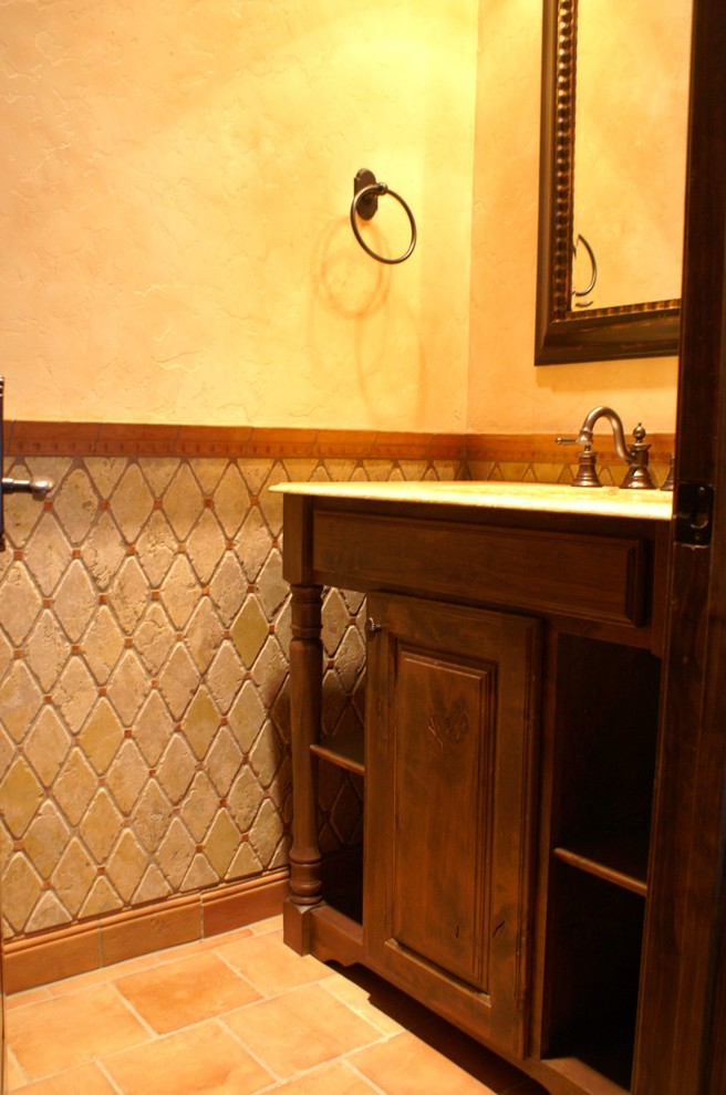 Réalisation d'une grande salle de bain principale méditerranéenne en bois foncé avec un placard avec porte à panneau surélevé, un carrelage beige, un carrelage de pierre, un mur beige, tomettes au sol, un lavabo encastré et un plan de toilette en granite.