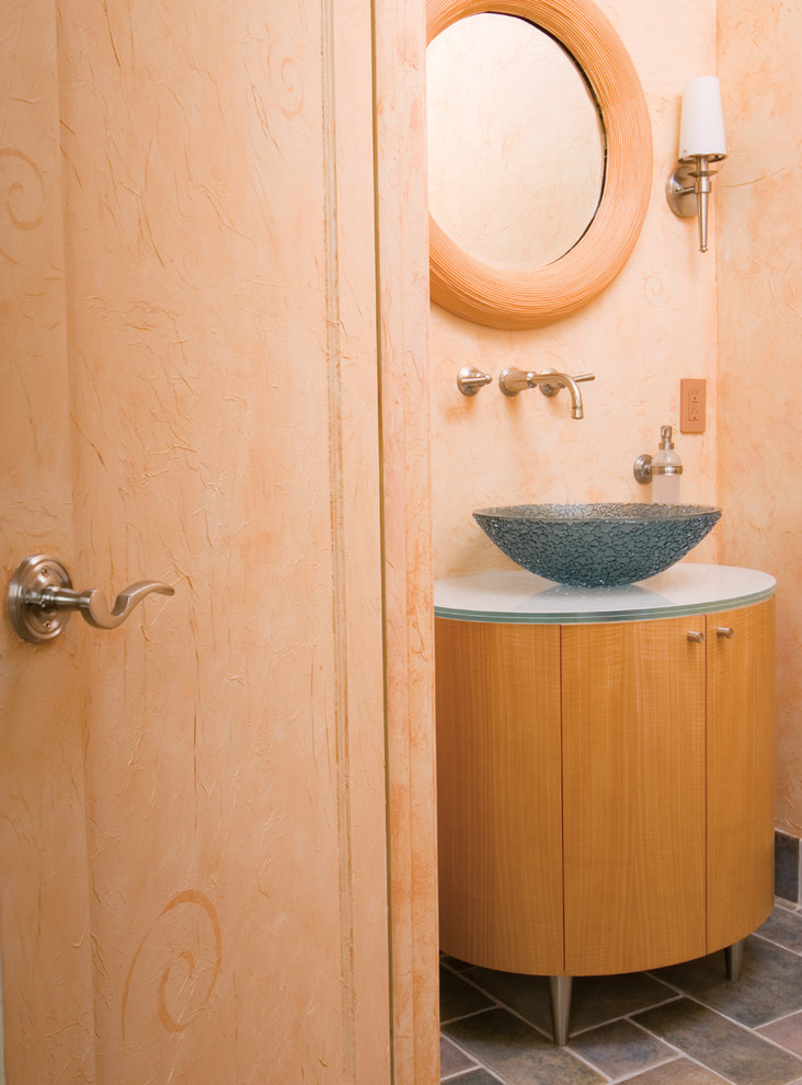 Modelo de cuarto de baño tradicional renovado pequeño con lavabo sobreencimera, puertas de armario de madera clara, paredes rosas, encimera de vidrio, encimeras blancas y armarios con paneles lisos