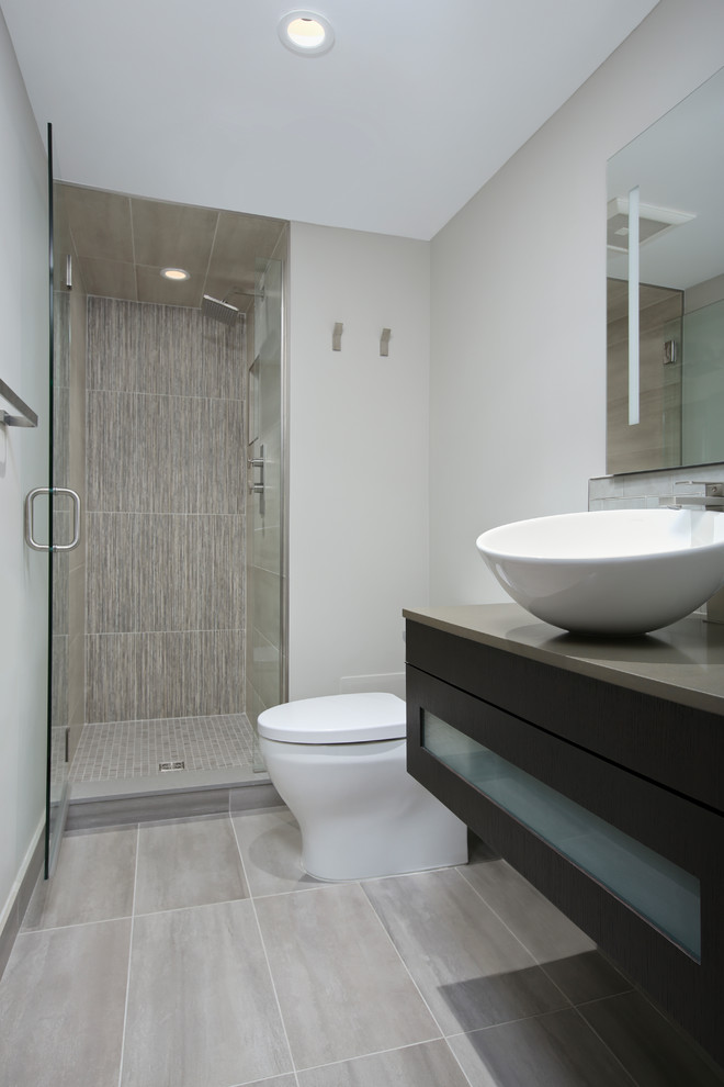 Medium sized contemporary shower room bathroom in Denver with glass-front cabinets, brown cabinets, an alcove shower, a one-piece toilet, grey tiles, porcelain tiles, beige walls, porcelain flooring, a vessel sink, engineered stone worktops, grey floors, a hinged door and grey worktops.