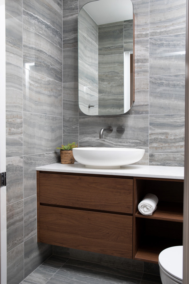 Idée de décoration pour une petite salle de bain design en bois brun avec WC à poser, un carrelage gris, des carreaux de porcelaine, un mur gris, un sol en carrelage de porcelaine, une vasque, un sol gris, un plan de toilette blanc, meuble simple vasque et meuble-lavabo suspendu.
