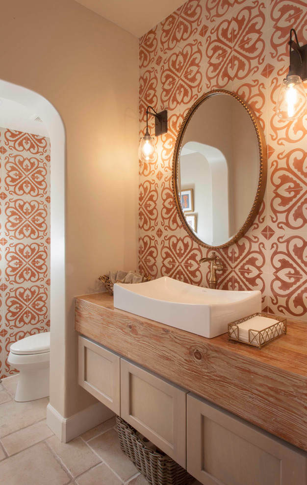 Idée de décoration pour une salle de bain tradition en bois clair avec un placard à porte shaker, un carrelage beige, un carrelage orange, un mur beige, une vasque, un plan de toilette en bois, un sol beige, un plan de toilette marron et des toilettes cachées.