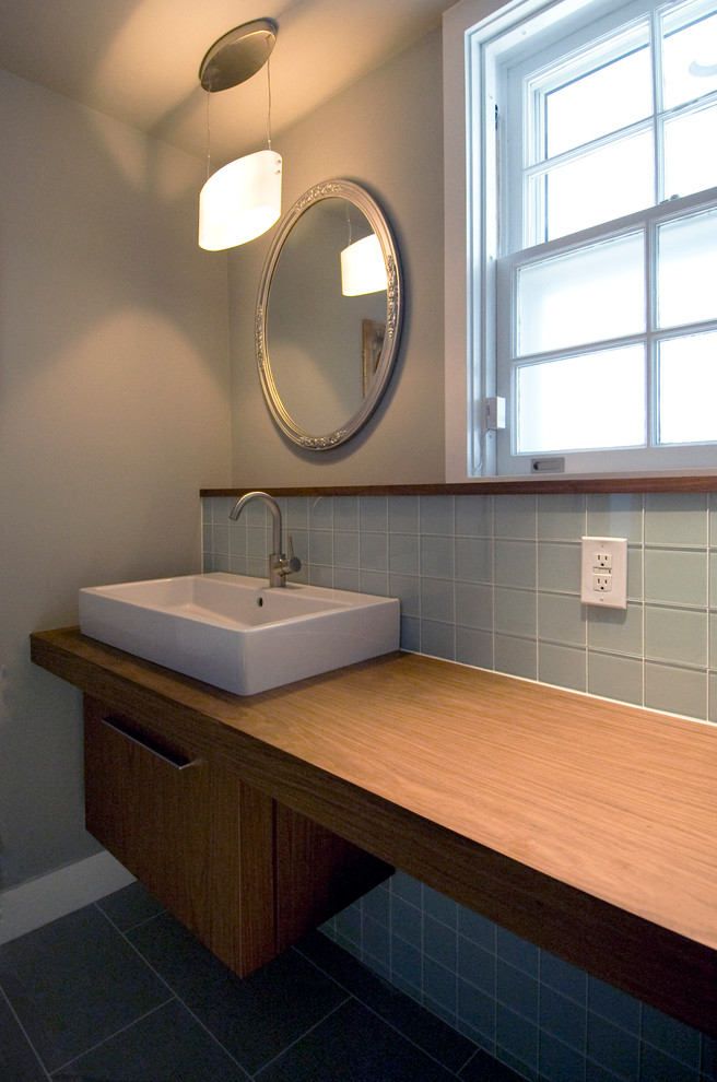 Immagine di una stanza da bagno minimalista con ante lisce, ante in legno scuro, piastrelle blu, lavabo a bacinella, top in legno e piastrelle di vetro