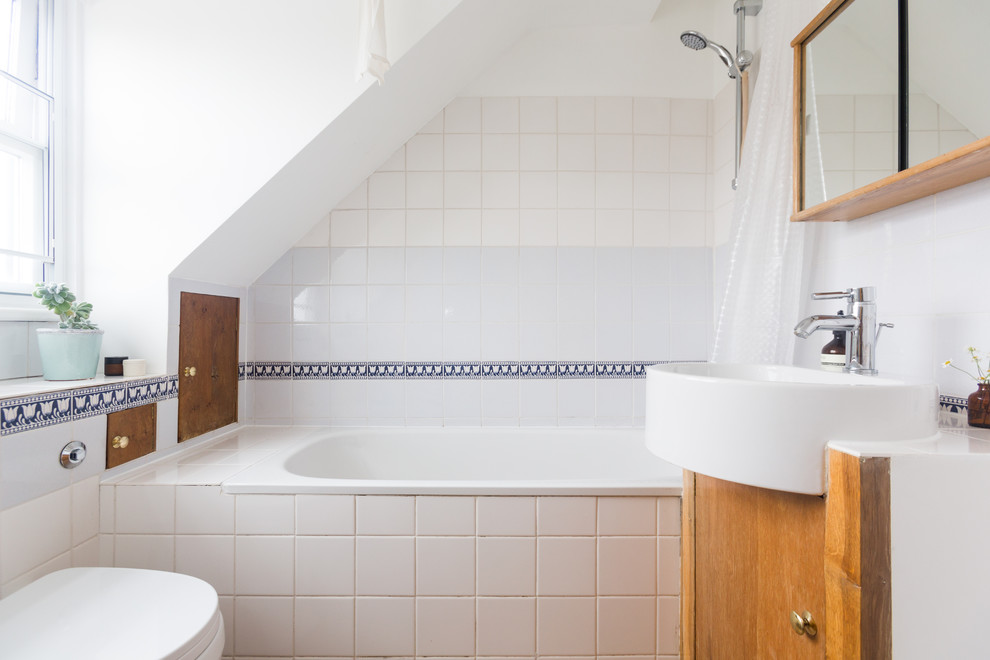 Design ideas for a scandi shower room bathroom in London with flat-panel cabinets, medium wood cabinets, a built-in bath, a shower/bath combination, a wall mounted toilet, white tiles, white walls, a console sink and a shower curtain.