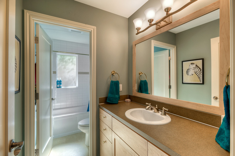Foto på ett vintage badrum, med ett nedsänkt handfat, skåp i ljust trä, laminatbänkskiva, ett badkar i en alkov, en dusch/badkar-kombination, en toalettstol med separat cisternkåpa, vit kakel, blå väggar och linoleumgolv