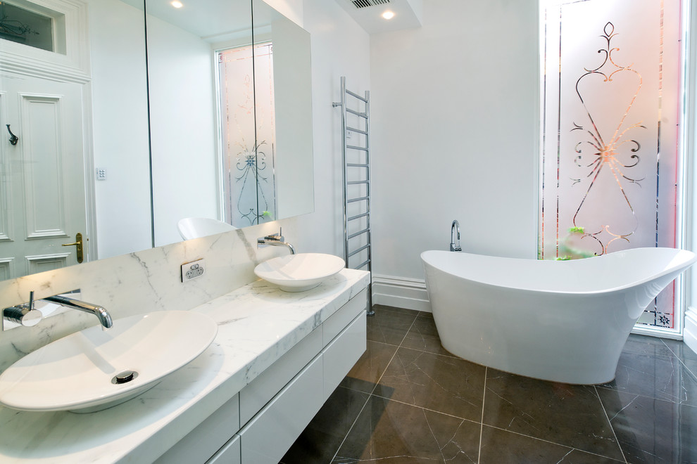 На фото: большая ванная комната в современном стиле с отдельно стоящей ванной, настольной раковиной, мраморной столешницей и тумбой под две раковины с