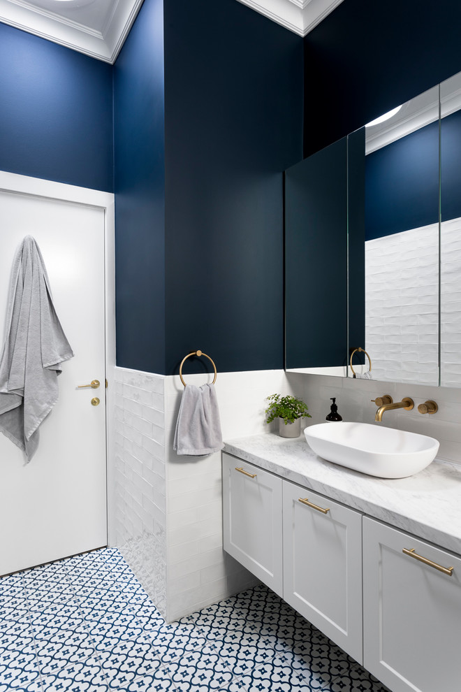 メルボルンにある中くらいなトランジショナルスタイルのおしゃれなマスターバスルーム (白いキャビネット、白いタイル、青い壁、ベッセル式洗面器、青い床、アンダーマウント型浴槽、シャワー付き浴槽	、大理石の洗面台、落し込みパネル扉のキャビネット、分離型トイレ、サブウェイタイル、磁器タイルの床、開き戸のシャワー) の写真