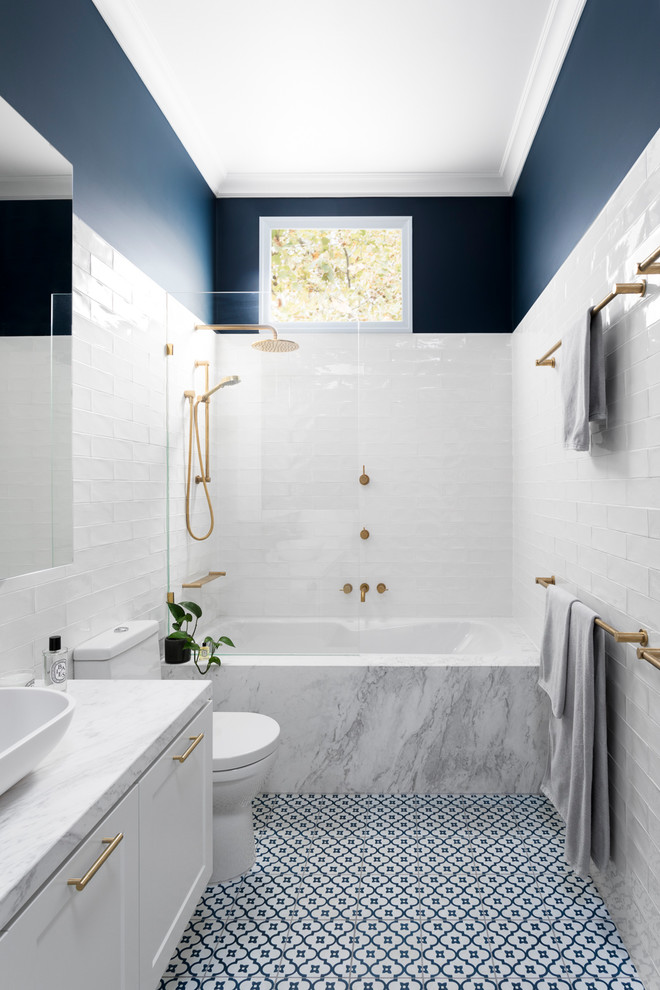 Inredning av ett klassiskt mellanstort grå grått en-suite badrum, med vita skåp, ett undermonterat badkar, en dusch/badkar-kombination, vit kakel, blå väggar, marmorbänkskiva, blått golv, luckor med infälld panel, en toalettstol med separat cisternkåpa, tunnelbanekakel, klinkergolv i porslin, ett fristående handfat och dusch med gångjärnsdörr