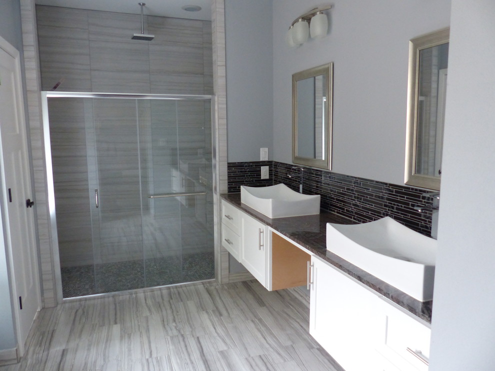 Modern inredning av ett stort en-suite badrum, med skåp i shakerstil, vita skåp, ett fristående badkar, en dusch i en alkov, grå kakel, glaskakel, grå väggar, vinylgolv, ett fristående handfat, granitbänkskiva, beiget golv och dusch med skjutdörr