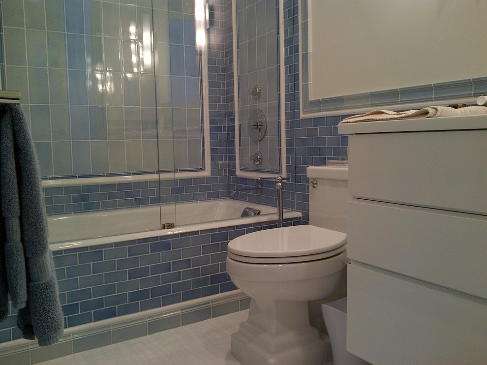 Idée de décoration pour une salle de bain principale design avec un placard à porte plane, des portes de placard blanches, une baignoire en alcôve, un combiné douche/baignoire, WC à poser, un carrelage bleu et des dalles de pierre.