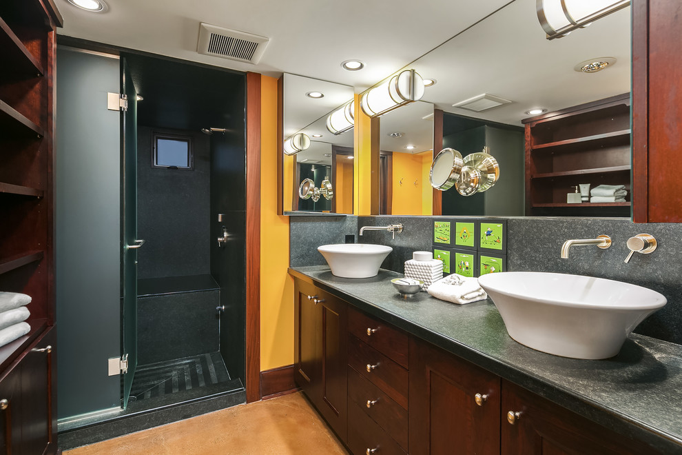 Пример оригинального дизайна: большая главная ванная комната в современном стиле с фасадами в стиле шейкер, темными деревянными фасадами, душем в нише, черной плиткой, плиткой из листового камня, желтыми стенами, бетонным полом, настольной раковиной, столешницей из талькохлорита, коричневым полом, душем с распашными дверями и черной столешницей