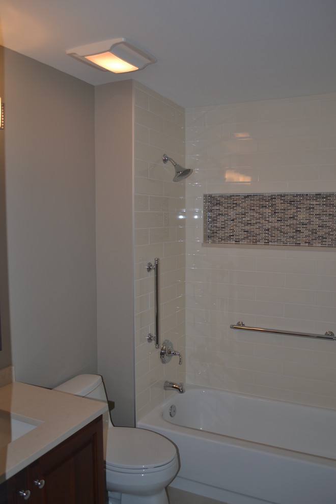 Cette image montre une douche en alcôve design en bois foncé de taille moyenne avec un placard avec porte à panneau surélevé, une baignoire en alcôve, WC à poser, un carrelage beige, des carreaux de porcelaine, un mur gris, un sol en carrelage de porcelaine, un lavabo encastré et un plan de toilette en quartz.