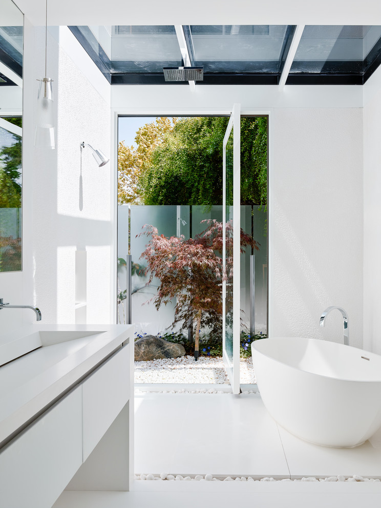 Пример оригинального дизайна: главная ванная комната среднего размера в стиле модернизм с плоскими фасадами, белыми фасадами, открытым душем, белой плиткой, каменной плиткой, белыми стенами, отдельно стоящей ванной, монолитной раковиной, открытым душем и белым полом