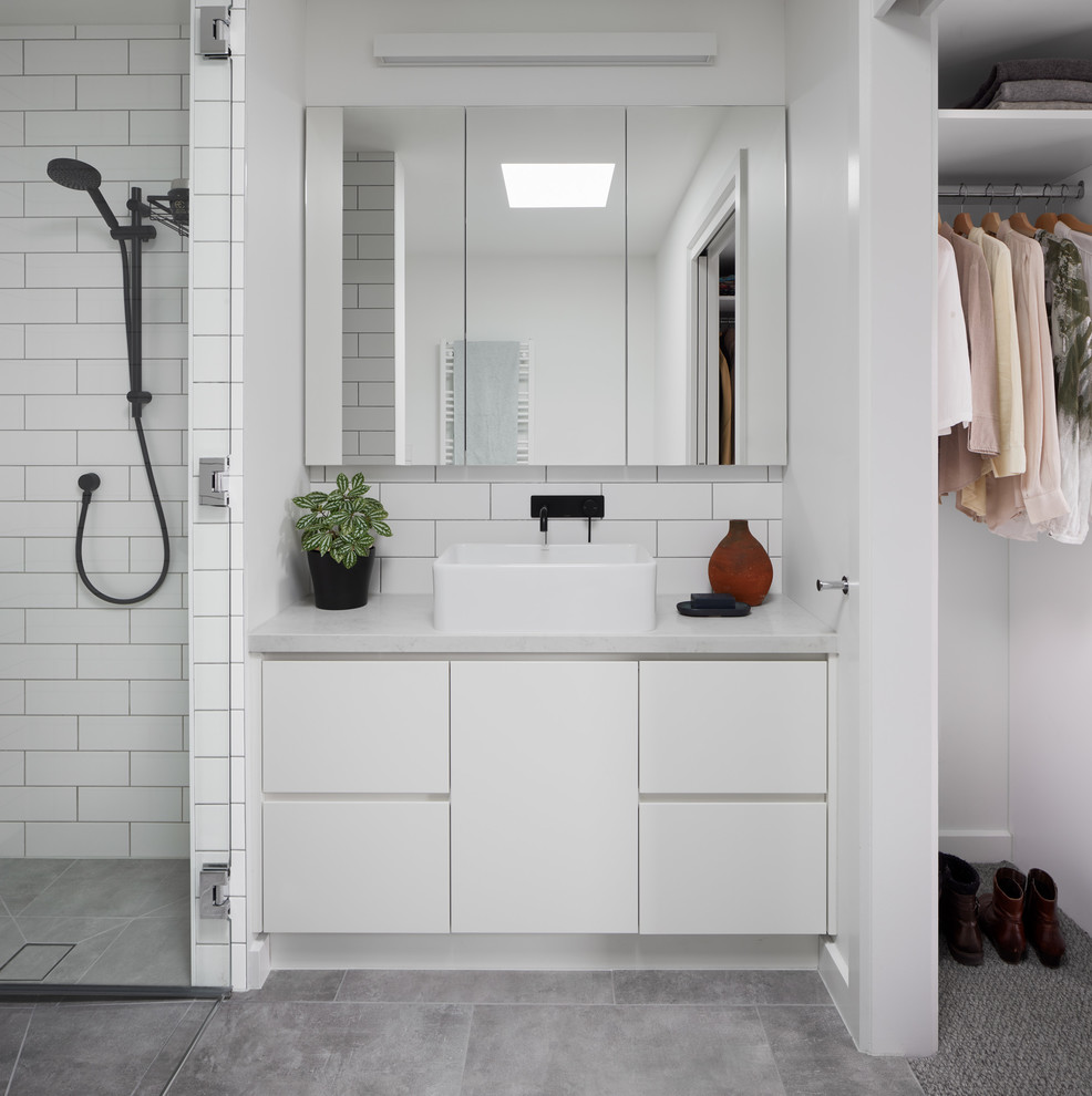 Bild på ett funkis grå grått badrum, med släta luckor, vita skåp, vit kakel, tunnelbanekakel, vita väggar, ett fristående handfat och grått golv