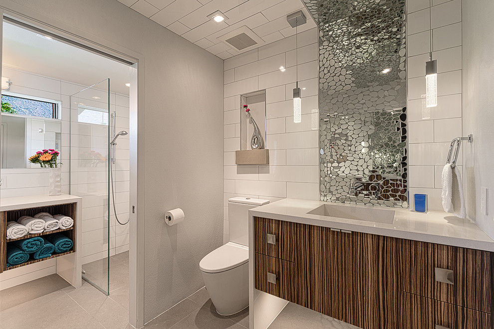 Großes Retro Badezimmer mit flächenbündigen Schrankfronten, hellbraunen Holzschränken, bodengleicher Dusche, Wandtoilette mit Spülkasten, grauen Fliesen, weißer Wandfarbe, Keramikboden, integriertem Waschbecken und Quarzit-Waschtisch in Los Angeles