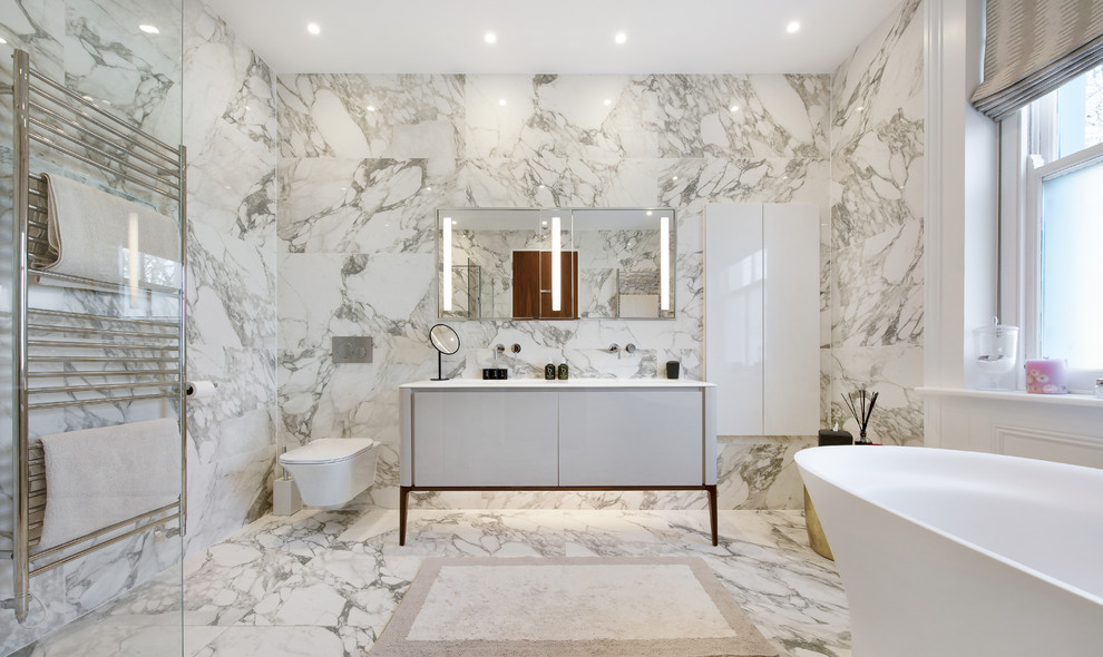 ロンドンにあるコンテンポラリースタイルのおしゃれなマスターバスルーム (フラットパネル扉のキャビネット、グレーのキャビネット、置き型浴槽、グレーのタイル、白いタイル、白い床、白い洗面カウンター) の写真